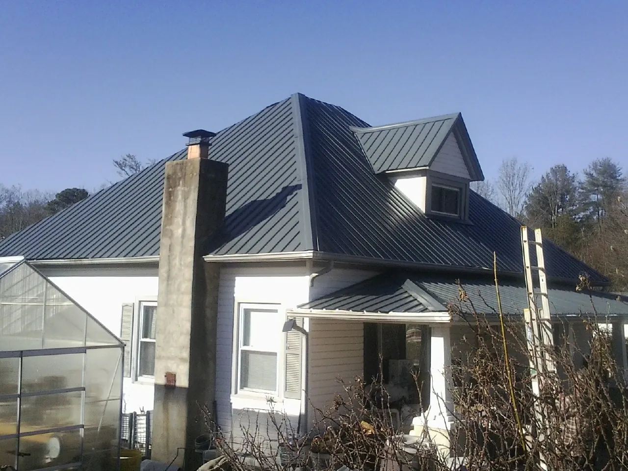 Dark blue standing seam metal roof on a white farmhouse with dormer — Slate & Tile Roof Repair by Roofing Brothers in Bat Cave