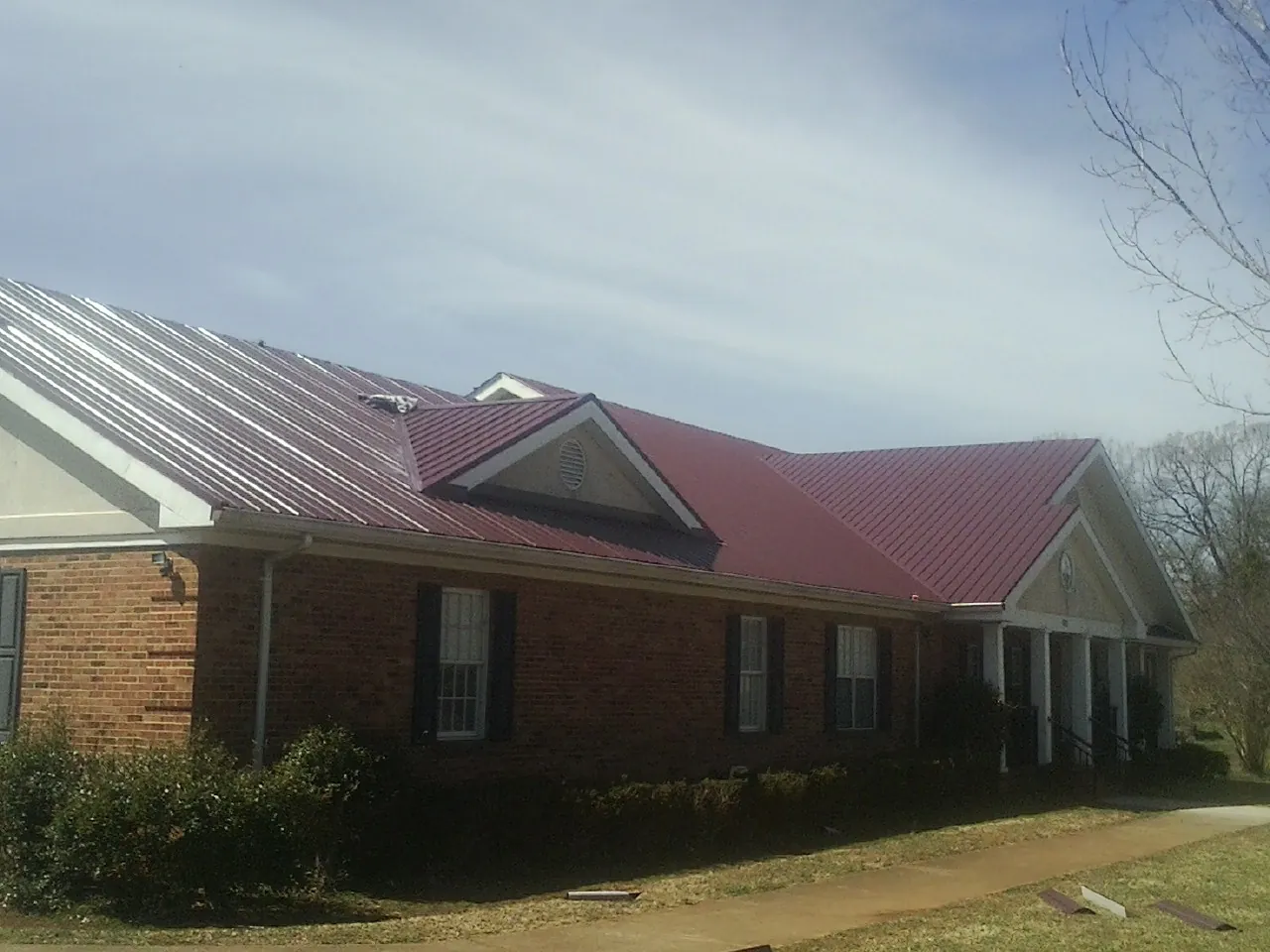 Red metal roof with gabled entries on a long brick building, from a Hail Damage Roof Repair job in Bat Cave