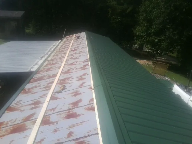 Old rusted panels beside newly installed green metal roofing — Wind Damage Roof Repair by Roofing Brothers in Bat Cave