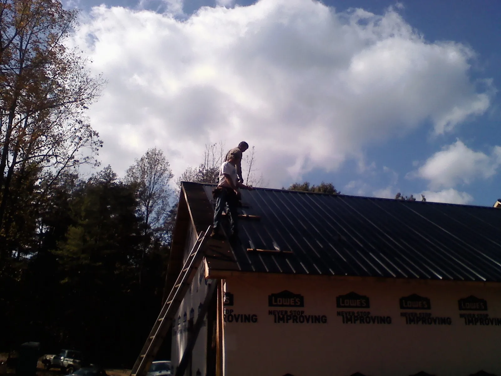 Roofer fastening dark metal panels high against a cloudy sky, from a Roof Inspection job in Bat Cave