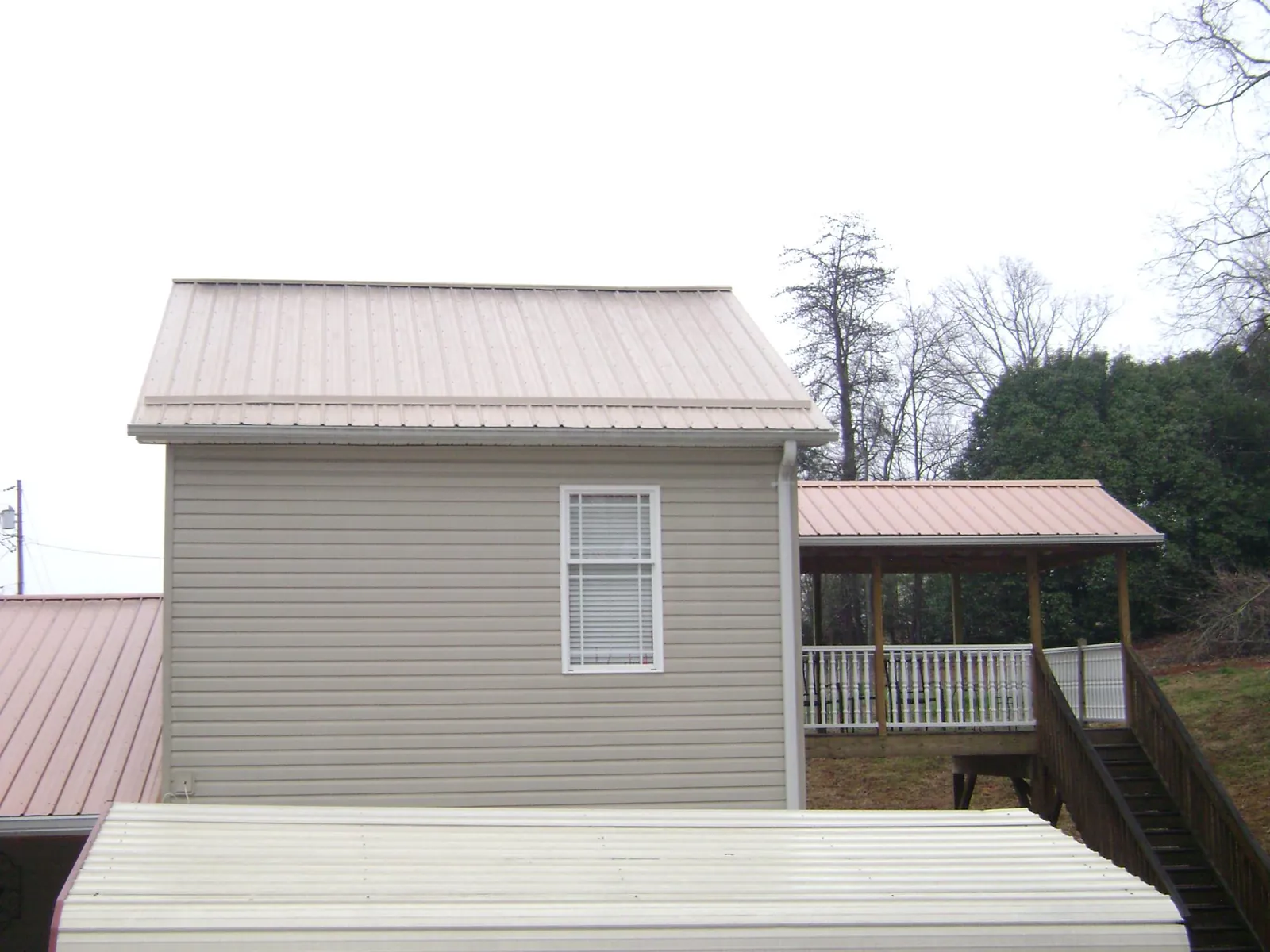 Tan metal roofs on a two story addition and attached porch, from a Roof Replacement job in Bat Cave